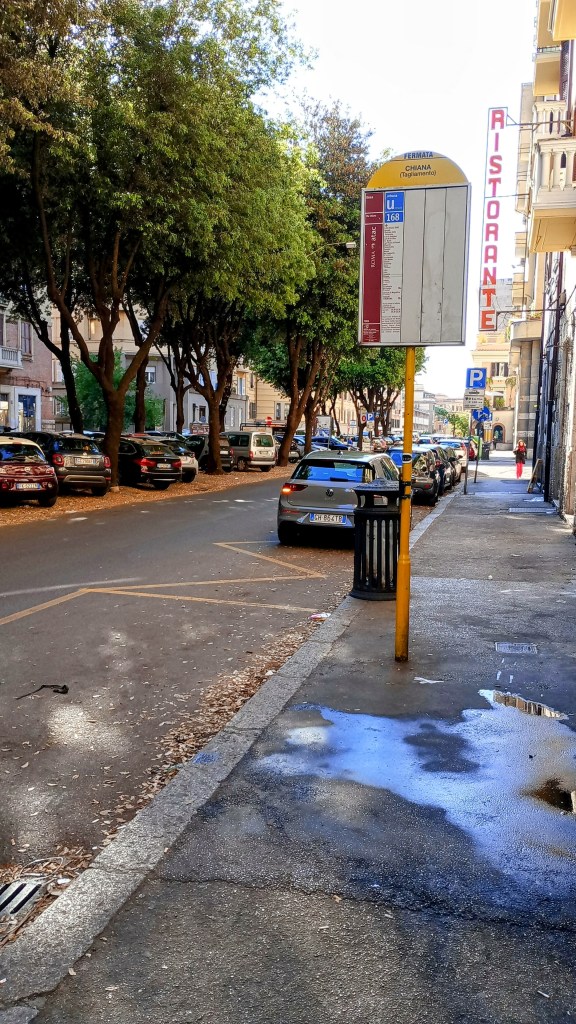 A tram stop across from a shaded parking area (via Chiana, Roma)