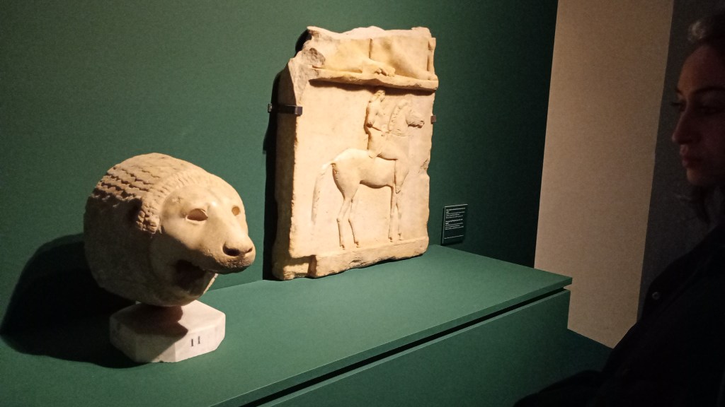 statue of a lion's head next to a stele with a man riding a horse