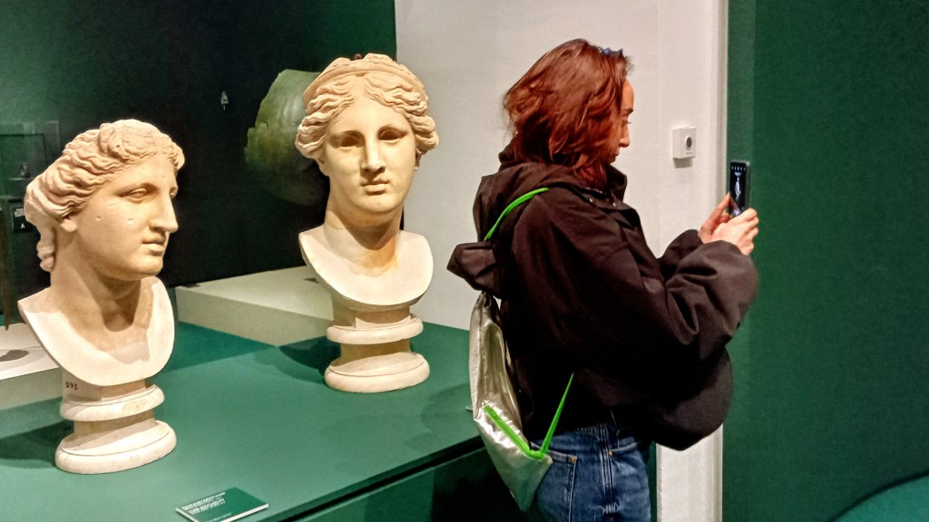 two marble busts and a young woman with a cell phone