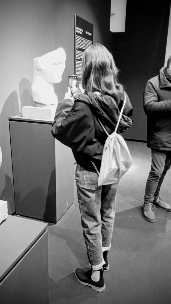 young woman taking a photo of a marble bust
