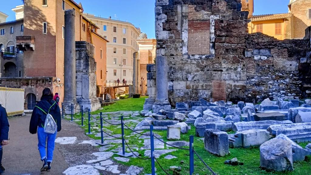 phto of broken columns on the ground and girl walking down a path